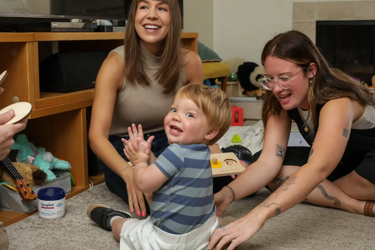 Speech therapist playing on the floor with a laughing toddler during a therapy session